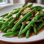 A close-up of bright green beans tossed in brown butter sauce and topped with slivered almonds: Green Bean Almondine with Brown Butter.