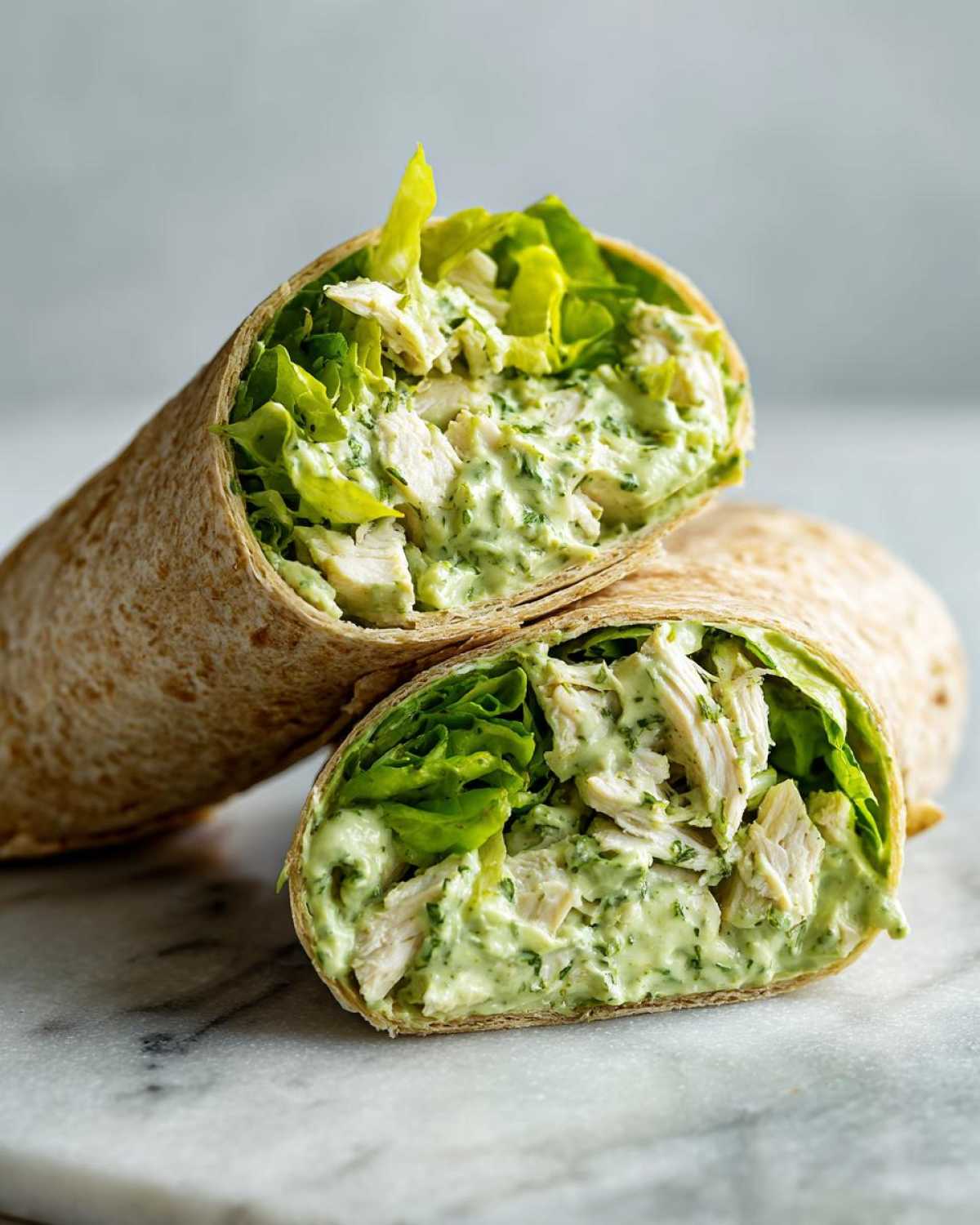 Close-up of Green Goddess Chicken Wraps cut in half, showing shredded chicken mixed with creamy green sauce and crisp lettuce.