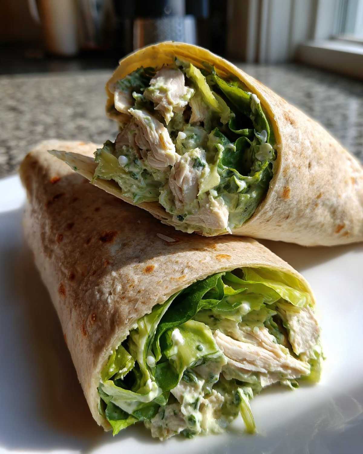 A whole wheat tortilla filled with shredded chicken, lettuce, and creamy Green Goddess Chicken Wraps filling, cut in half.