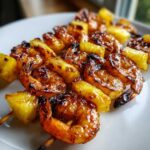 Close-up of perfectly caramelized Grilled Pineapple Shrimp Skewers resting on a white plate.