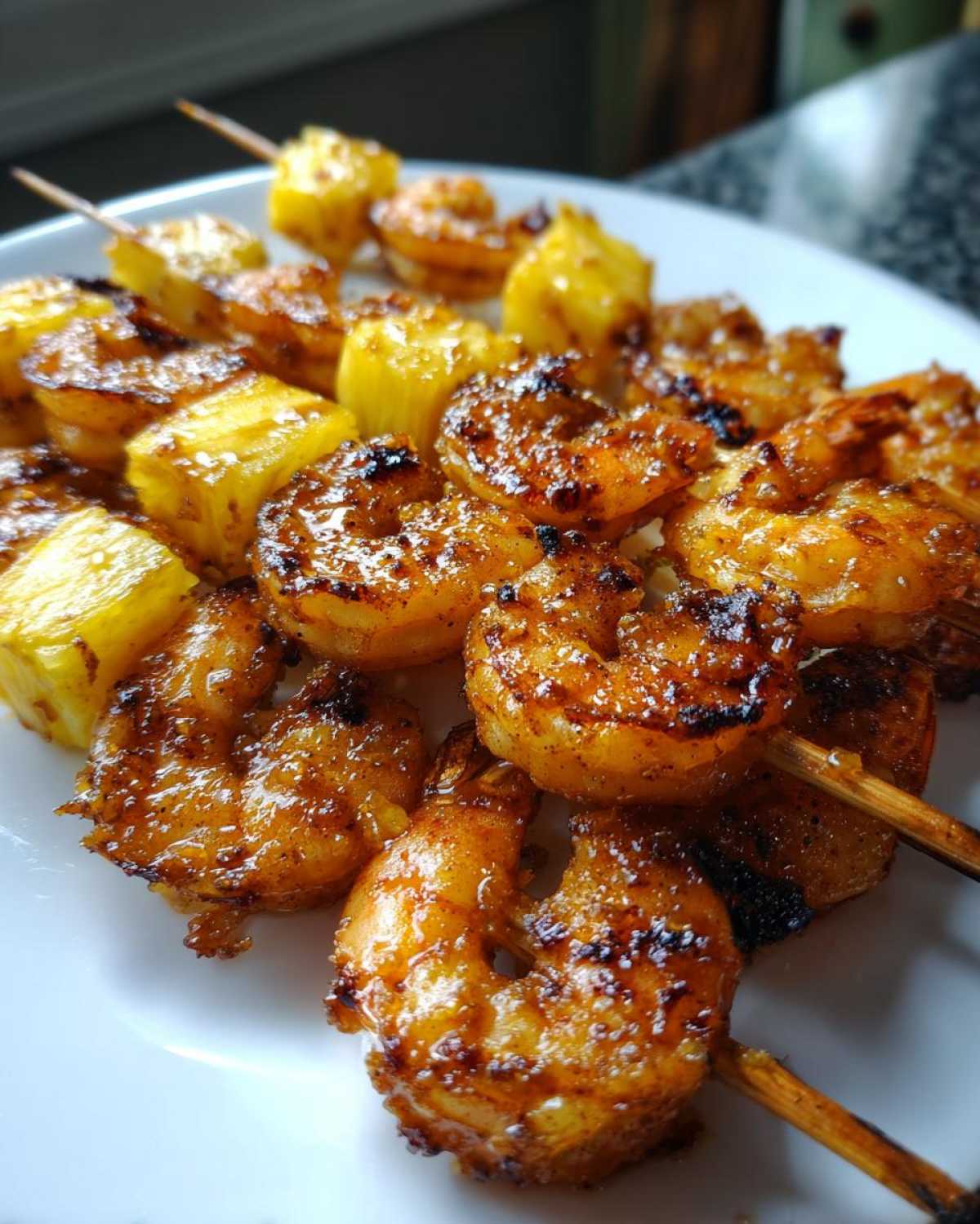 Close-up of perfectly caramelized Grilled Pineapple Shrimp Skewers arranged on a white plate.
