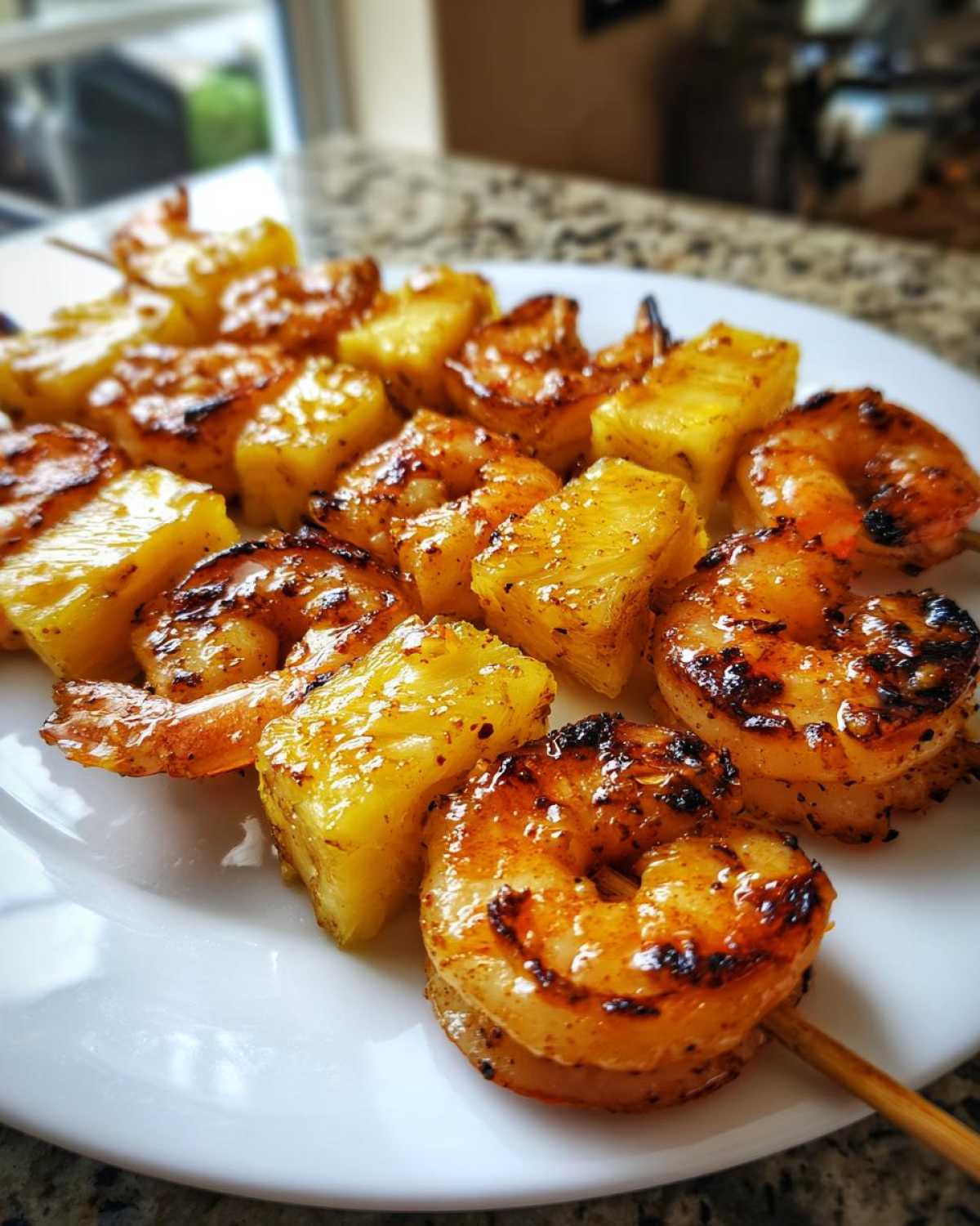 Close-up of perfectly grilled pineapple shrimp skewers, showing caramelized shrimp and juicy pineapple chunks on a white plate.