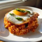 A perfectly plated mound of orange Kimchi Fried Rice topped with a crispy fried egg and sliced green onions.