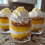 Three layered Lemon Curd Parfait Cups featuring lemon curd, cream, and graham cracker crust, topped with whipped cream and zest.