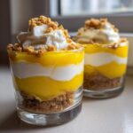 Two layered Lemon Curd Parfait Cups featuring bright yellow lemon curd, white cream, and a graham cracker crust, topped with whipped cream.