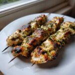 Close-up of three Lemon Herb Grilled Chicken Skewers resting on a white plate, showing char marks and green herb coating.