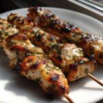 Three perfectly grilled Lemon Herb Chicken Skewers resting on a white plate, showing char marks and green herbs.