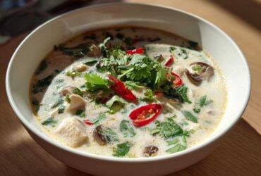 A close-up of a white bowl filled with creamy Lemongrass Coconut Chicken Soup, topped with cilantro and red chili slices.