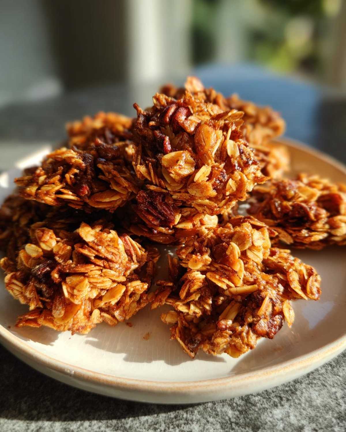A close-up shot of several golden brown Maple Pecan Granola Clusters piled on a light-colored plate.