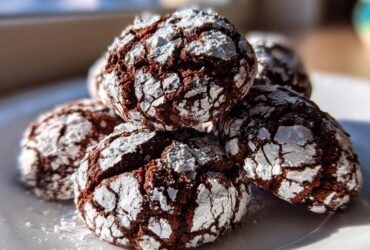 Close-up of several rich, dark Mexican Chocolate Crinkle Cookies heavily dusted with cracked powdered sugar on a white plate.