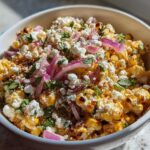 A bowl filled with vibrant Mexican Street Corn Salad Elote Style, topped generously with cotija cheese, red onion, and cilantro.