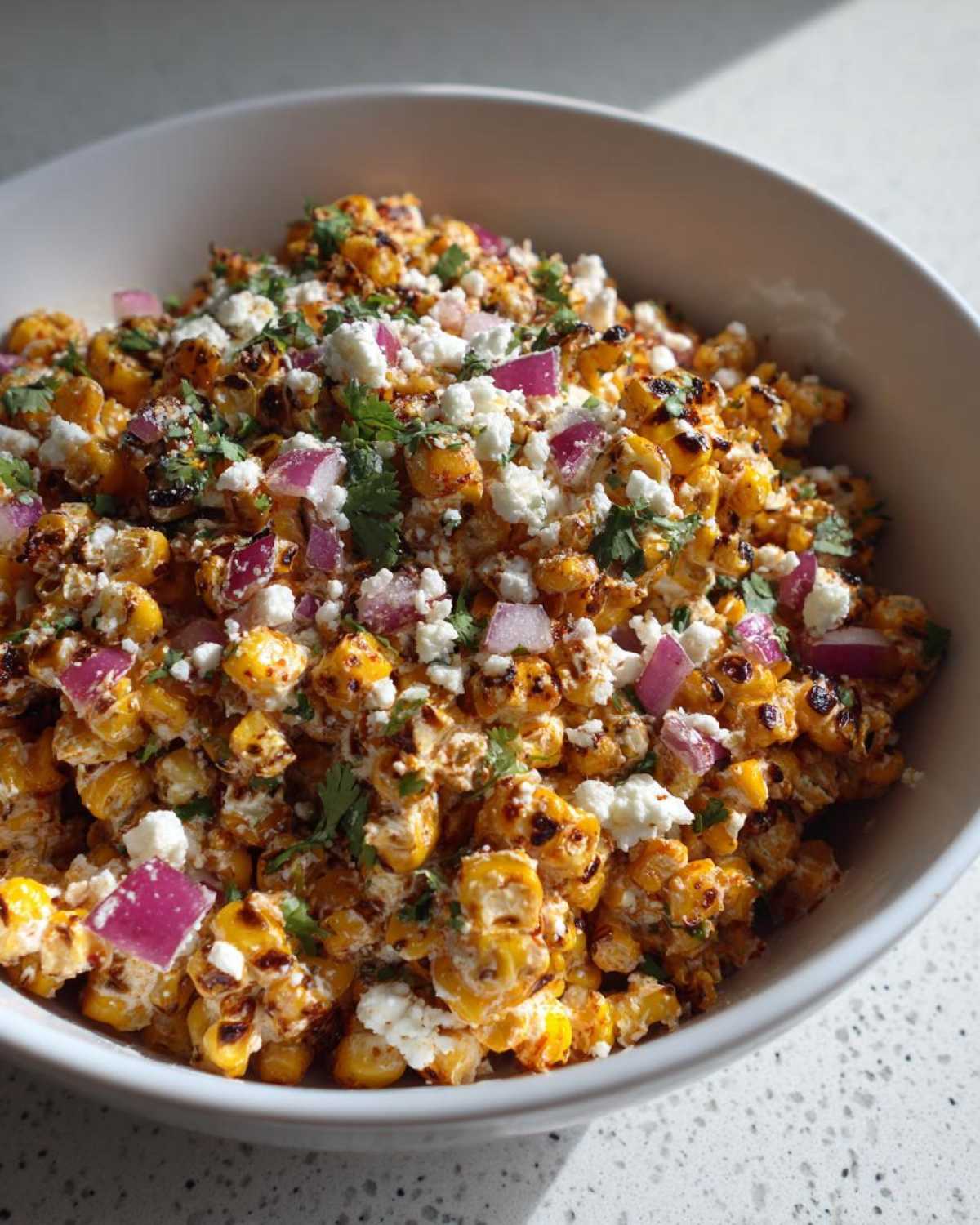 Close-up of Mexican Street Corn Salad Elote Style in a white bowl, topped with cotija cheese, red onion, and cilantro.