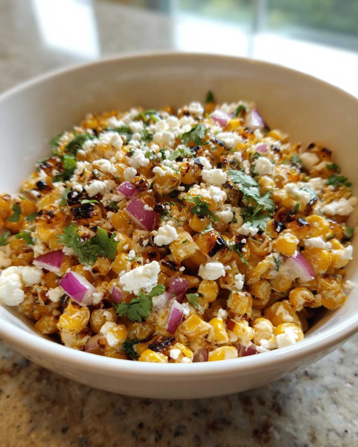Close-up of Mexican Street Corn Salad Elote Style in a white bowl, topped with cotija cheese and cilantro.