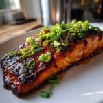 A perfectly cooked fillet of Miso Glazed Salmon with Scallions, featuring a dark, caramelized glaze and fresh green onion topping.