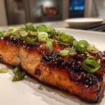 A perfectly cooked fillet of Miso Glazed Salmon with Scallions, featuring a dark, shiny glaze and topped with fresh green scallion rings.