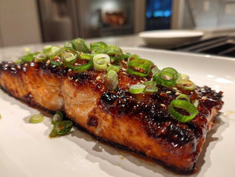 A perfectly cooked fillet of Miso Glazed Salmon with Scallions, featuring a dark, shiny glaze and topped with fresh green scallion rings.