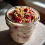 Close-up of No-Bake Strawberry Cheesecake Overnight Oats topped with fresh strawberries and graham cracker crumbs in a glass jar.