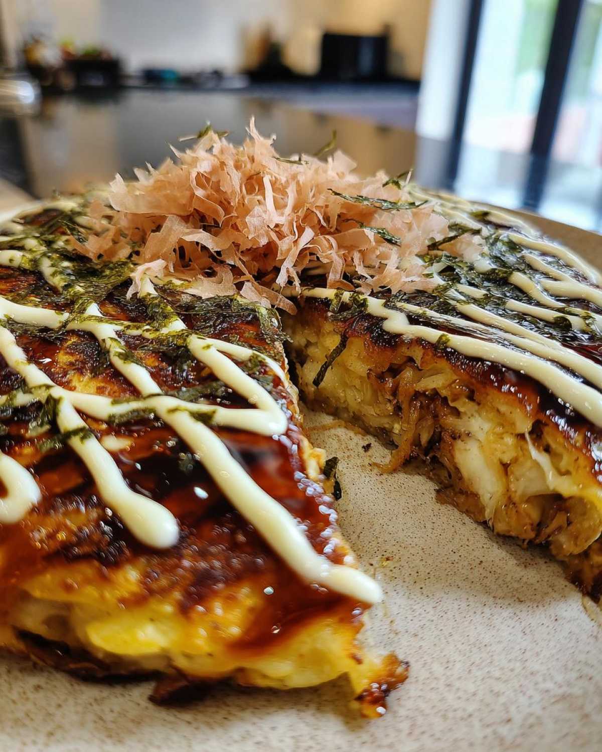 A thick slice cut from a fully dressed Okonomiyaki Cabbage Pancake, topped with bonito flakes, seaweed, and mayonnaise.