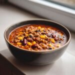 Close-up of a dark bowl filled with rich One-Pot Taco Soup with Lime, showing ground meat, corn, and kidney beans.