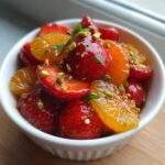 Close-up of a vibrant Orange Blossom Fruit Salad featuring glazed strawberries, orange segments, and chopped pistachios.