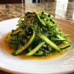 A vibrant mound of Pea Shoot Cucumber Salad tossed in a light dressing and topped with toasted sesame seeds.