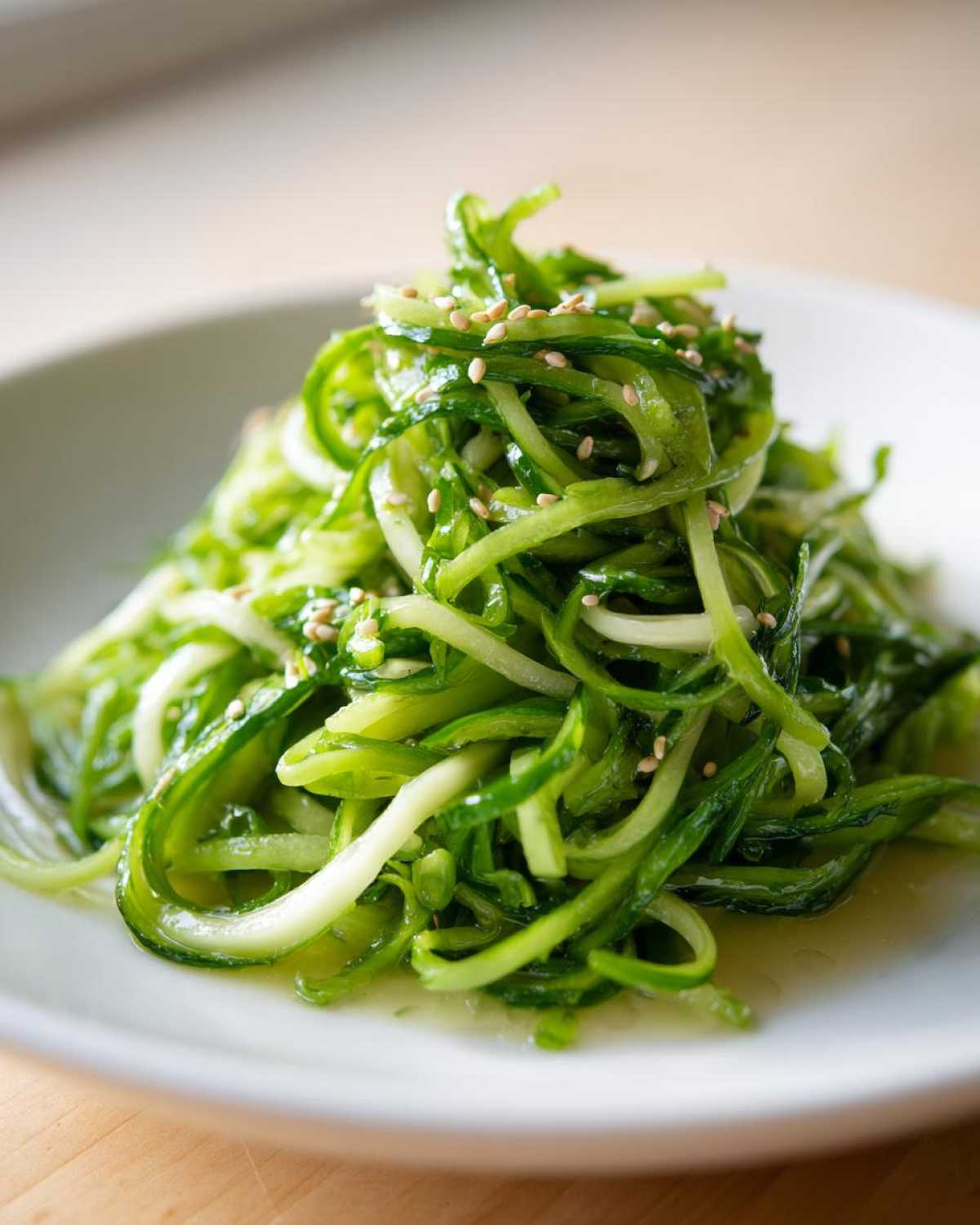 Close-up of spiralized cucumber noodles tossed with pea shoots and sesame seeds in a light dressing for Pea Shoot Cucumber Salad.