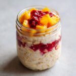 Close-up of Peach Melba Overnight Oats layered with creamy oats, raspberry sauce, and fresh peach chunks in a glass jar.