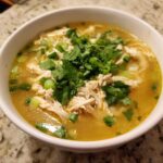 Close-up of a white bowl filled with Pho Ga Chicken Noodle Soup, featuring shredded chicken, broth, and fresh cilantro and green onions.