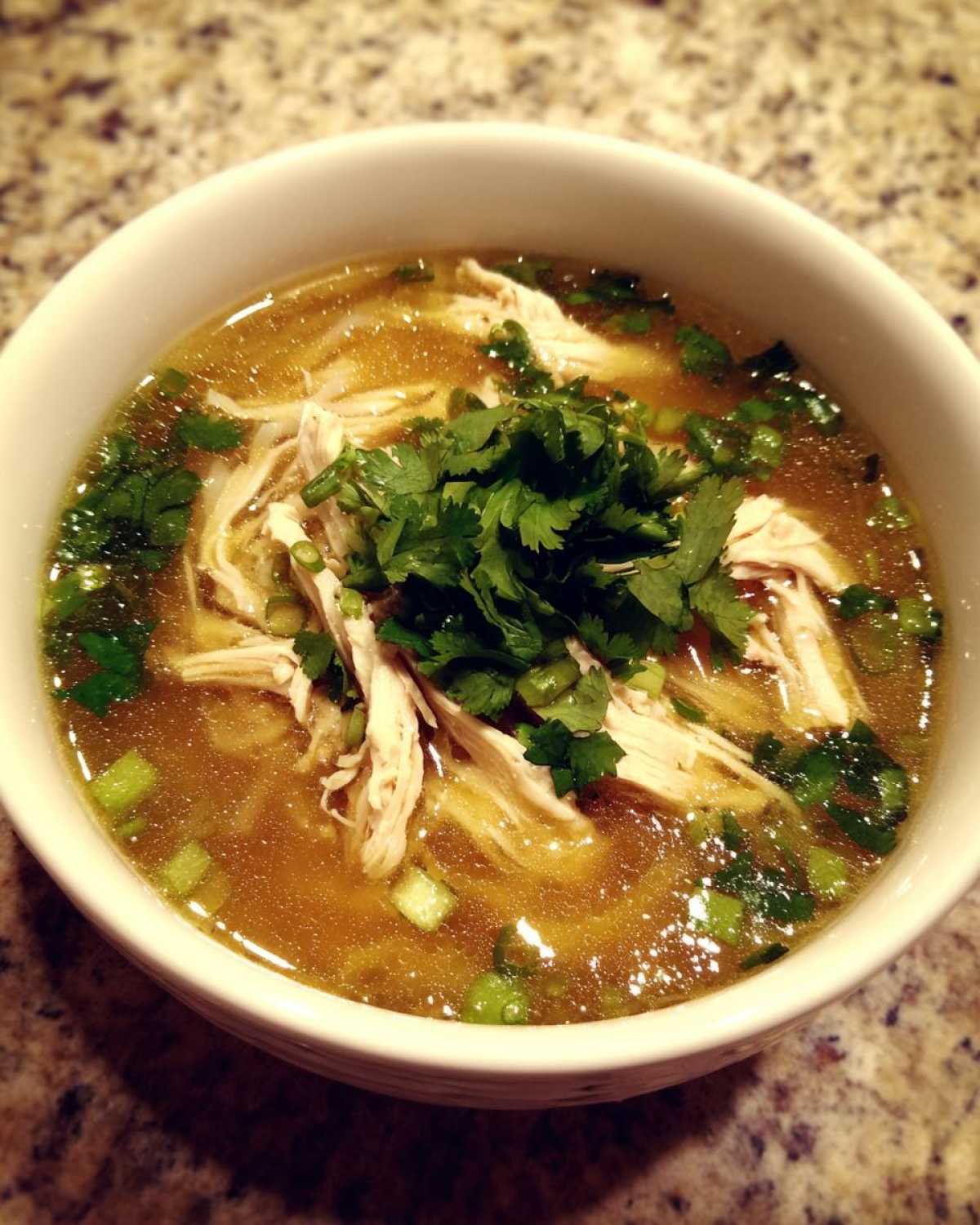 A close-up of a white bowl filled with rich broth, shredded chicken, and topped with fresh cilantro for Pho Ga Chicken Noodle Soup.
