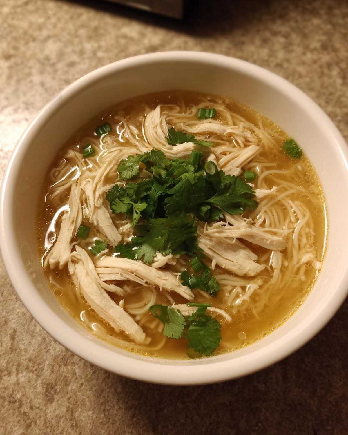 Overhead view of a white bowl filled with Pho Ga Chicken Noodle Soup, featuring shredded chicken, noodles, and fresh cilantro.