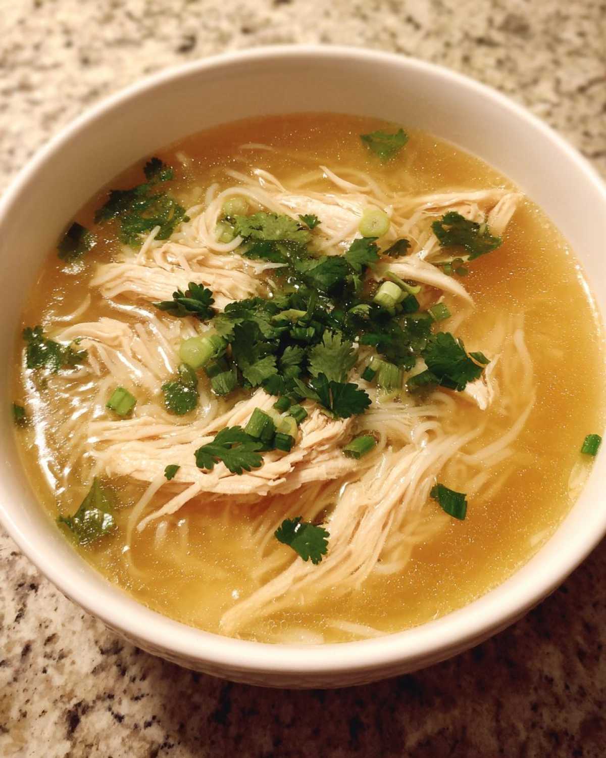 Close-up of a white bowl filled with Pho Ga Chicken Noodle Soup, featuring shredded chicken, rice noodles, and fresh cilantro.