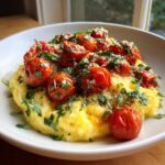 A close-up of creamy Polenta with Burst Tomatoes and Basil, topped with fresh herbs and Parmesan cheese.