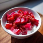 Close-up of bright pink, cubed rhubarb ginger compote served over white yogurt in a small bowl.