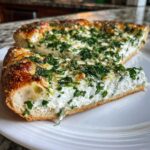 A thick slice of Ricotta Herb Brunch Pizza showing a creamy white ricotta filling topped generously with fresh green herbs on a white plate.