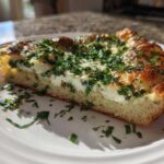 A thick slice of Ricotta Herb Brunch Pizza showing a fluffy crust, creamy ricotta, and a generous topping of fresh green herbs.