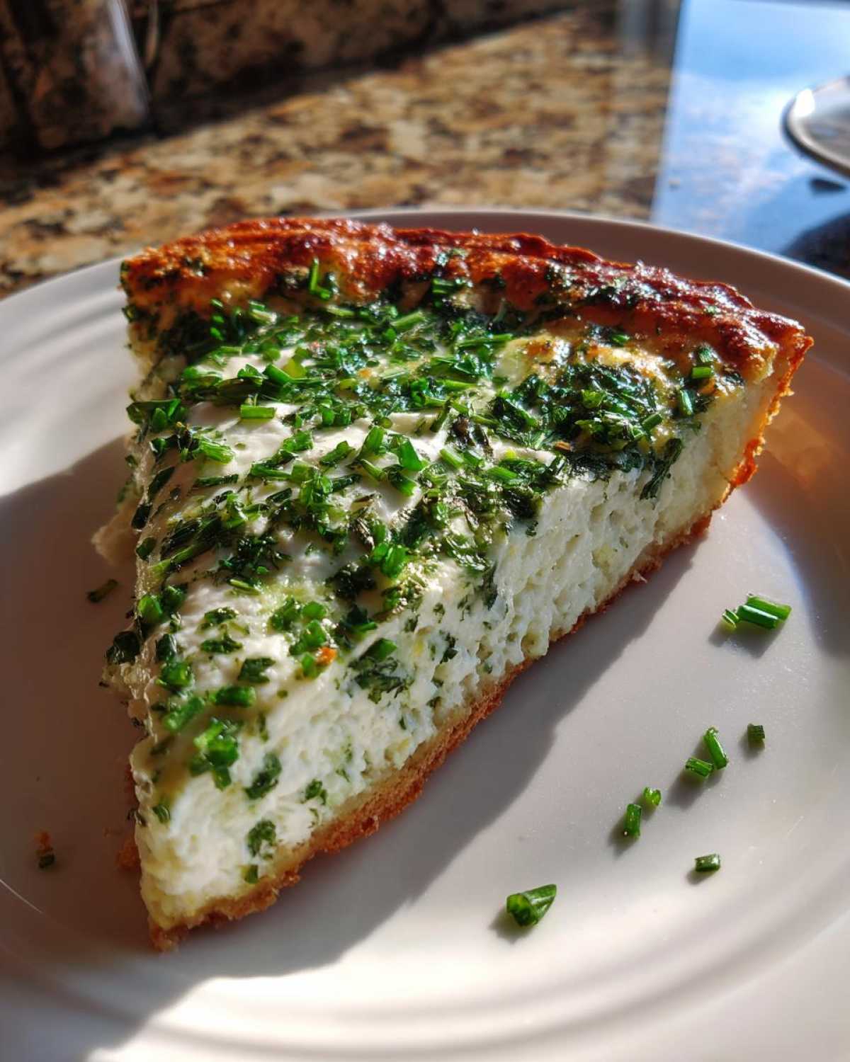 A thick slice of Ricotta Herb Brunch Pizza showing a creamy white filling topped generously with fresh green chives.