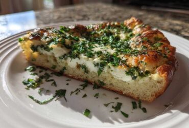A thick slice of Ricotta Herb Brunch Pizza showing a fluffy crust, creamy ricotta, and a generous topping of fresh green herbs.