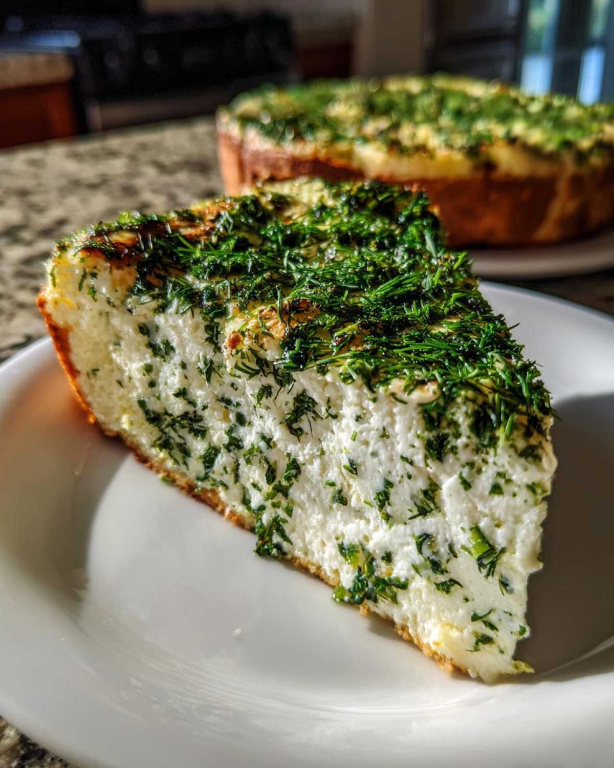 Close-up of a thick slice of Ricotta Herb Brunch Pizza, showing creamy white filling packed with green herbs, topped heavily with fresh dill.