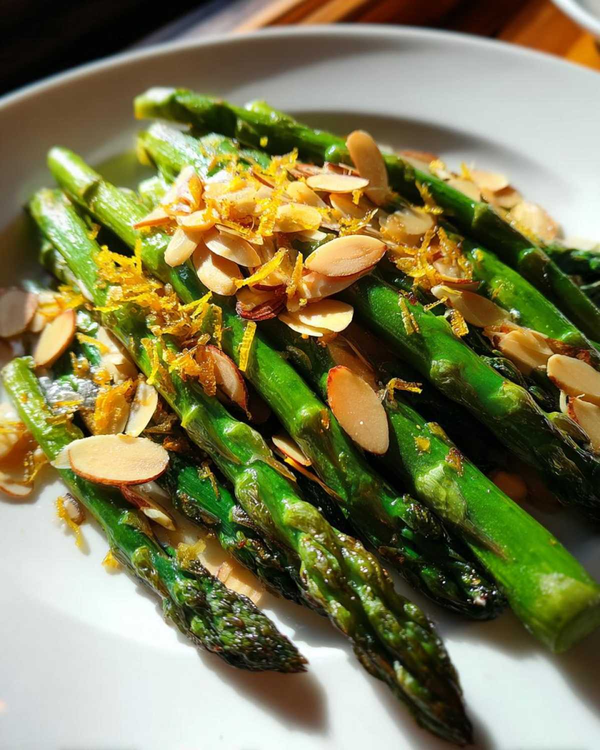 Close-up of bright green Roasted Asparagus with Almond Crunch, topped with slivered almonds and lemon zest.