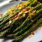 Close-up of bright green Roasted Asparagus with Almond Crunch, topped with slivered almonds and orange zest.