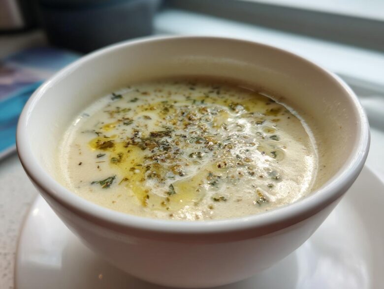Close-up of creamy Roasted Garlic White Bean Soup topped with olive oil and herbs in a white bowl.