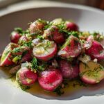 Close-up of roasted radishes with garlic and dill, glistening in oil on a white plate.