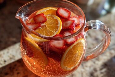 Close-up of a glass pitcher filled with Rose Strawberry Sangria Mocktail, garnished with bright orange slices and fresh strawberries.