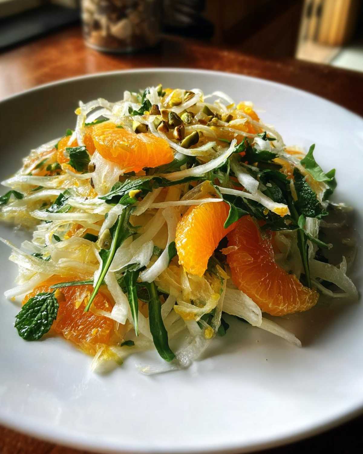 A bright serving of Shaved Fennel Citrus Salad featuring thinly sliced fennel, orange segments, arugula, and chopped pistachios.