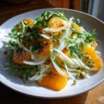 A bright Shaved Fennel Citrus Salad featuring orange segments, thinly sliced fennel, arugula, and pistachios on a white plate.