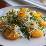 Close-up of a Shaved Fennel Citrus Salad featuring bright orange segments, white shaved fennel, and green pistachios on a white plate.
