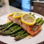 A perfectly cooked fillet of salmon served over roasted asparagus, topped with lemon slices for Sheet-Pan Salmon with Asparagus.