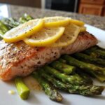 A cooked fillet of salmon topped with lemon slices resting on a bed of roasted asparagus, ready to eat.