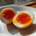 Two halves of a perfectly cooked Shoyu Ramen Eggs Overnight on a white plate, showing jammy, bright orange yolks.