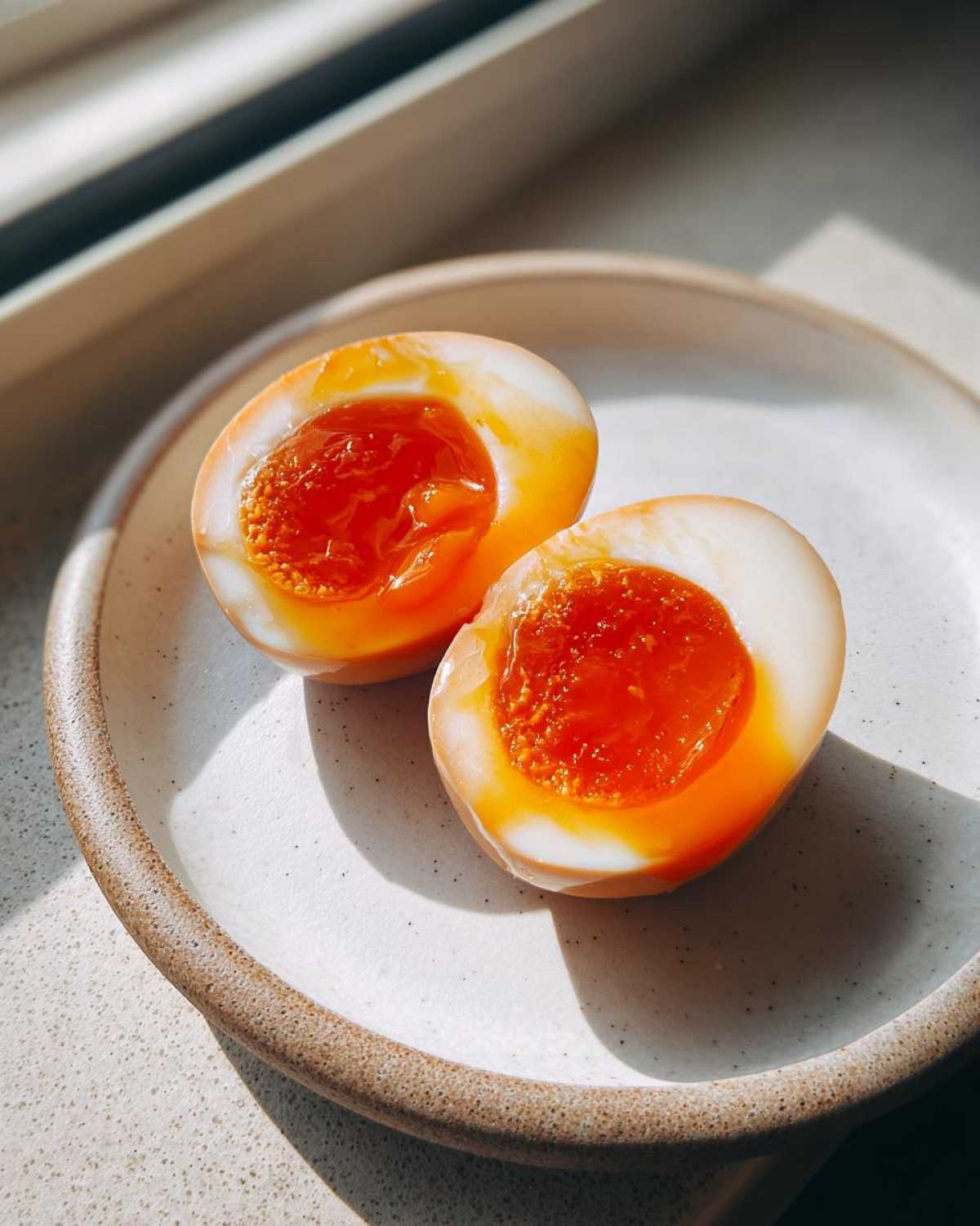 Two halves of a perfectly marinated Shoyu Ramen Eggs Overnight showing jammy, bright orange yolks on a speckled ceramic plate.